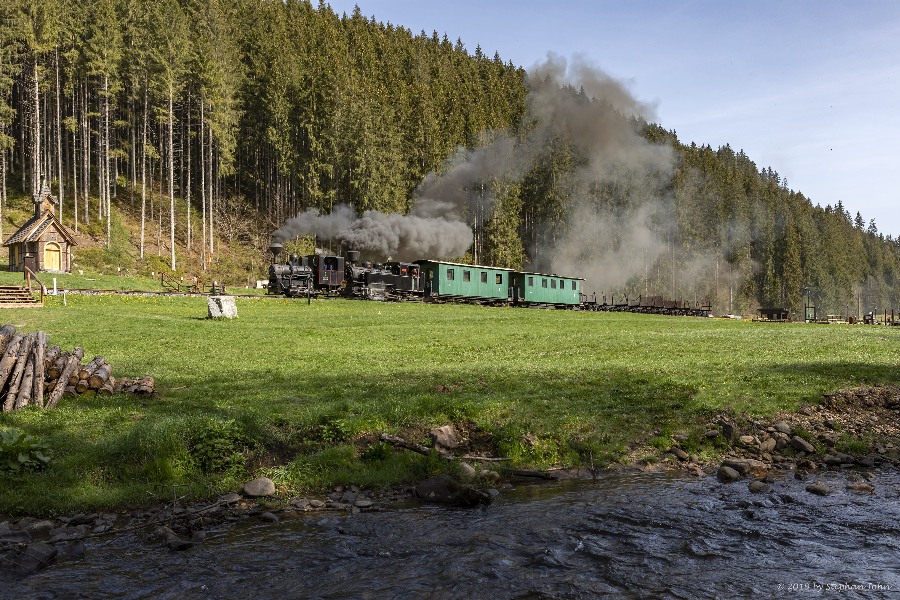 <p>Ein Zug der Waldbahn dampft mit zwei Lokomotiven die Strecke in Richtung Vydrovo entlang</p>