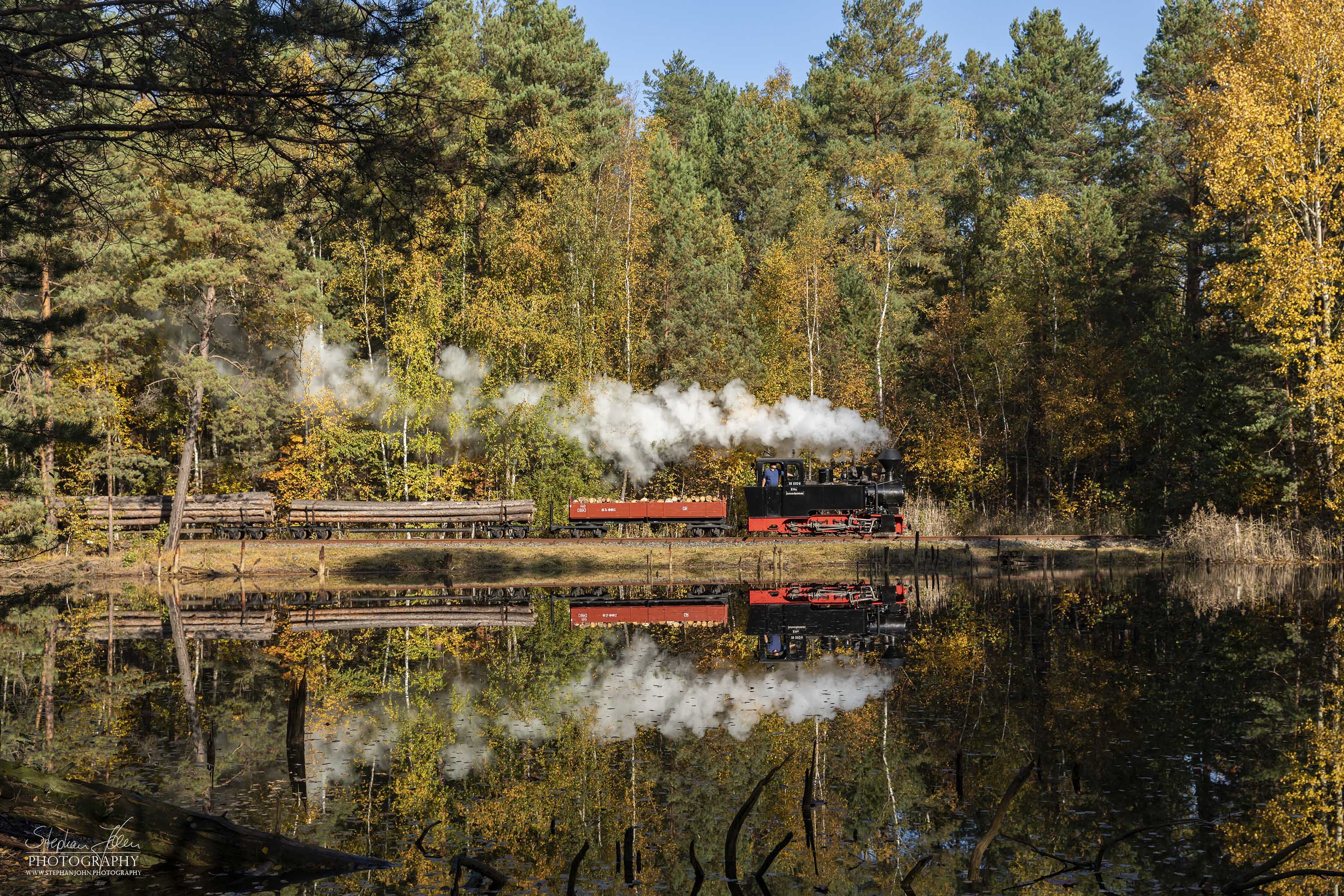 Lok 99 3312 fährt mit einem Holzzug bei bestem Wetter durch den bunten Herbstwald nach Weißwasser