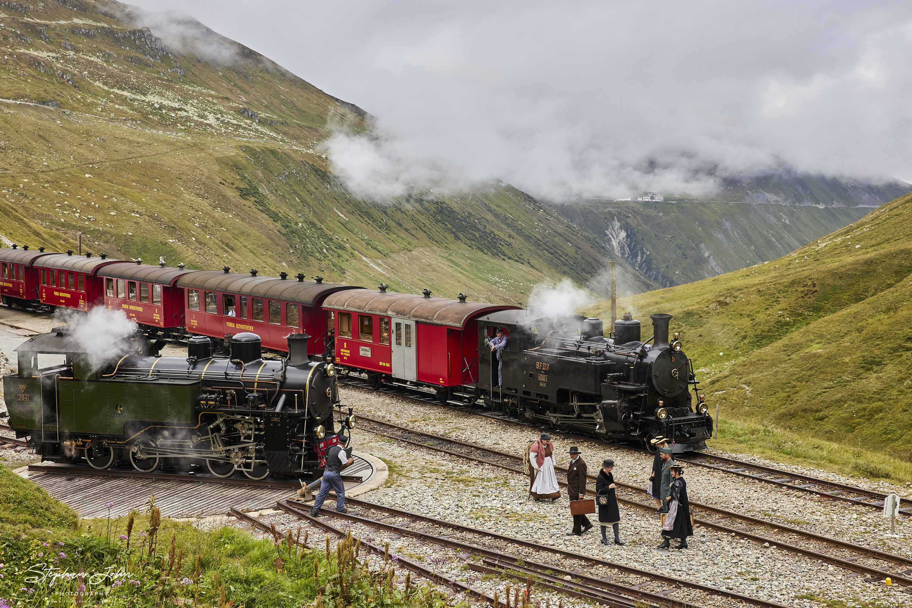 <p>Bahnhof Furka in 2.163 Meter Höhe. Der Güterzug hat abgespannt und der Personenzug nach Oberwald hat Aufenthalt. Die Reisenden nutzen die Zeit um das Drehen der Güterzuglokok anzuschauen.</p>
