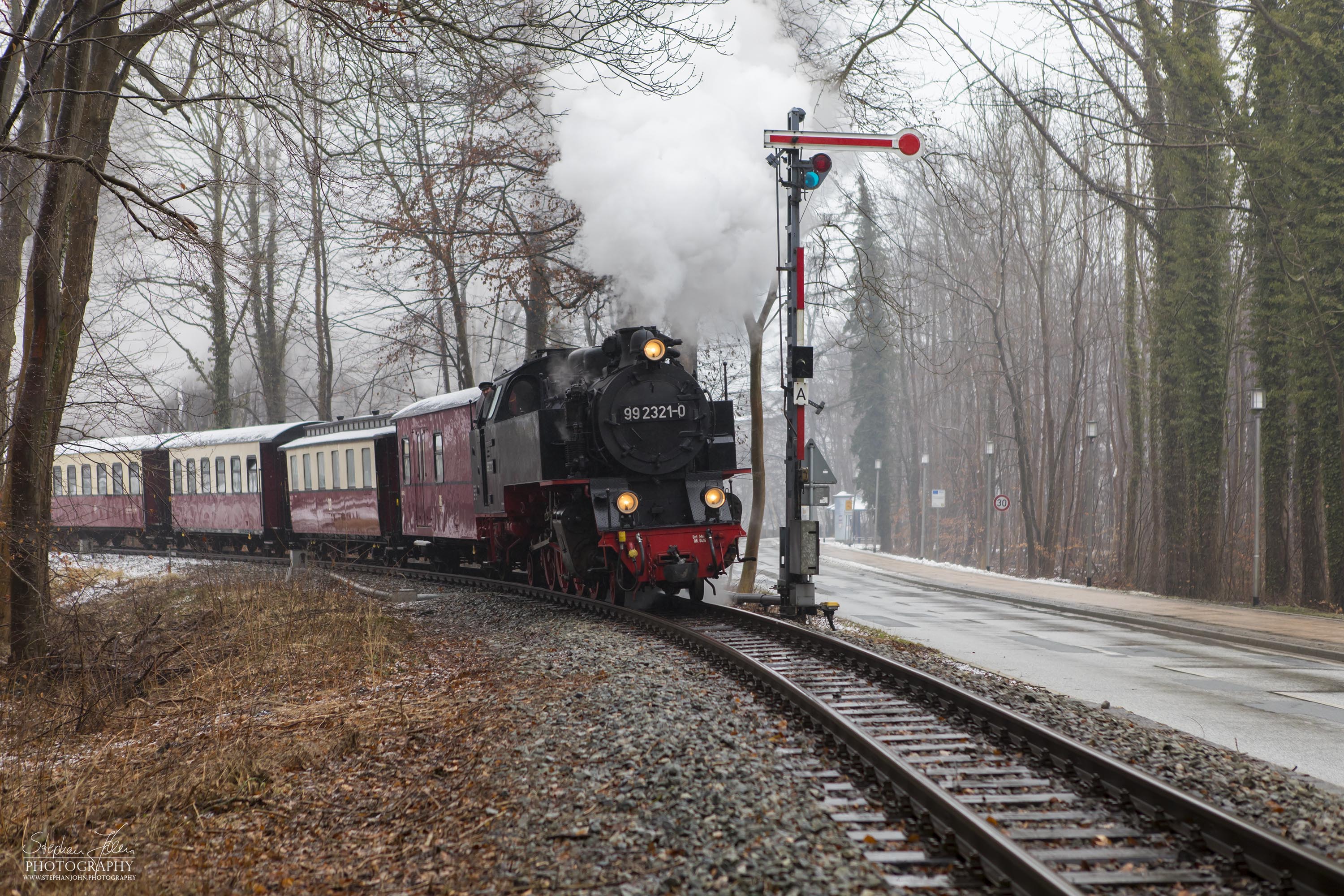 Lok 99 2321-0 mit einem Personenzug der Epoche IV während der Ausfahrt aus dem Bahnhof  Heiligendamm. Als Einfahrtsignal steht ein sogenanntes Negativsignal, da ggü. den anderen Formsignalen die Farben Rot und Weiß zur besseren Sichtbarkeit vertauscht sind. Die Zugbildung entspricht der Zeit zwischen 1980 und 1983, als die Personenwagen modernisiert wurden.