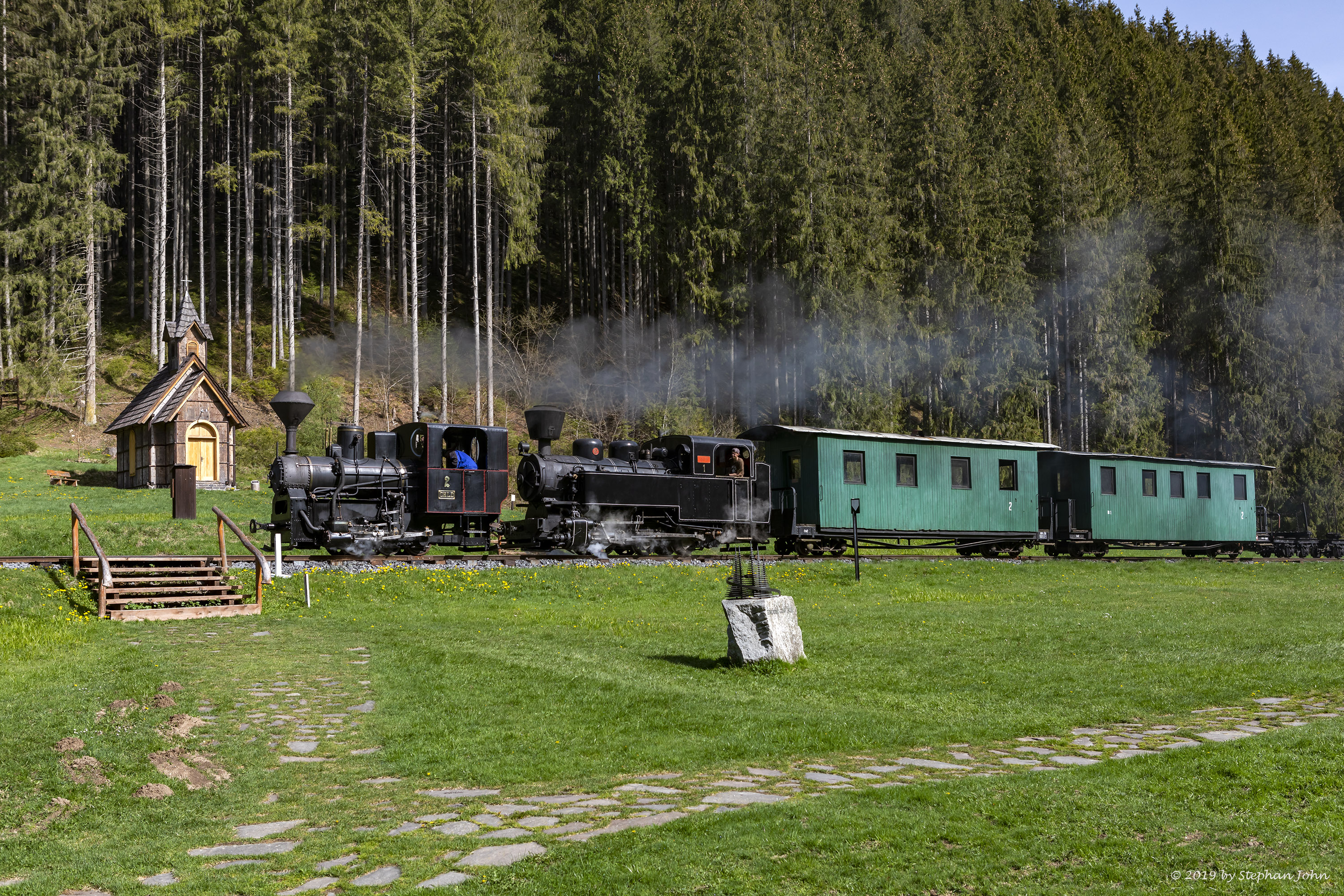 <p>Ein Zug der Waldbahn dampft mit zwei Lokomotiven die Strecke in Richtung Vydrovo entlang</p>