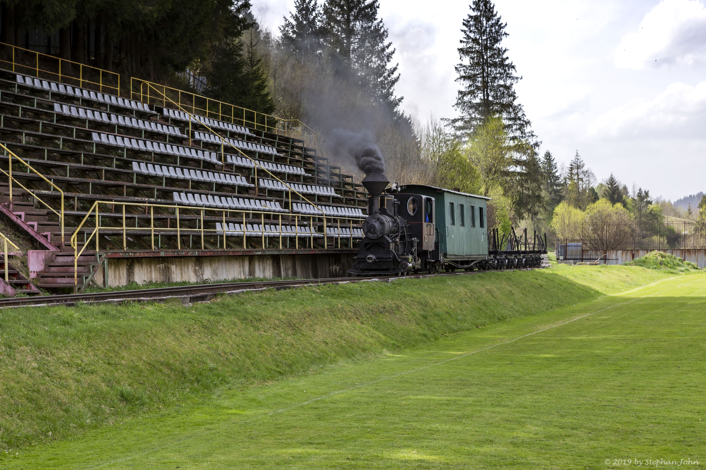 <p>Ein leerer Holzzug der Waldbahn Čierny Balog fährt durch das Fußballstadion des TJ Tatran Čierny Balog</p>