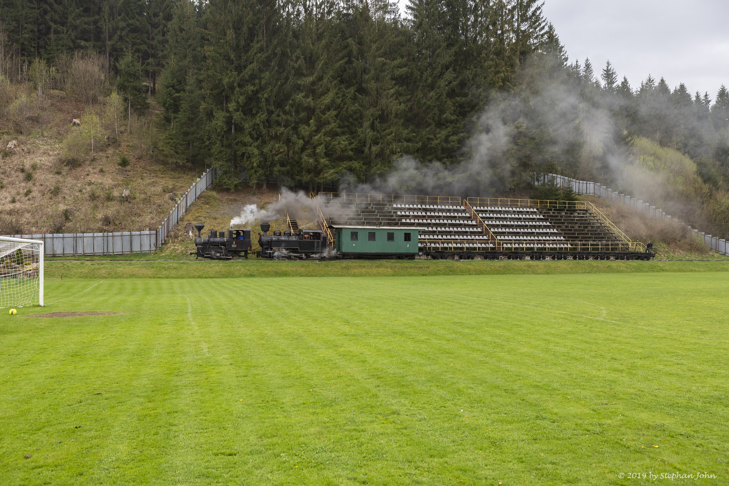 Ein leerer Holzzug der Waldbahn Čierny Balog fährt durch das Fußballstadion des TJ Tatran Čierny Balog