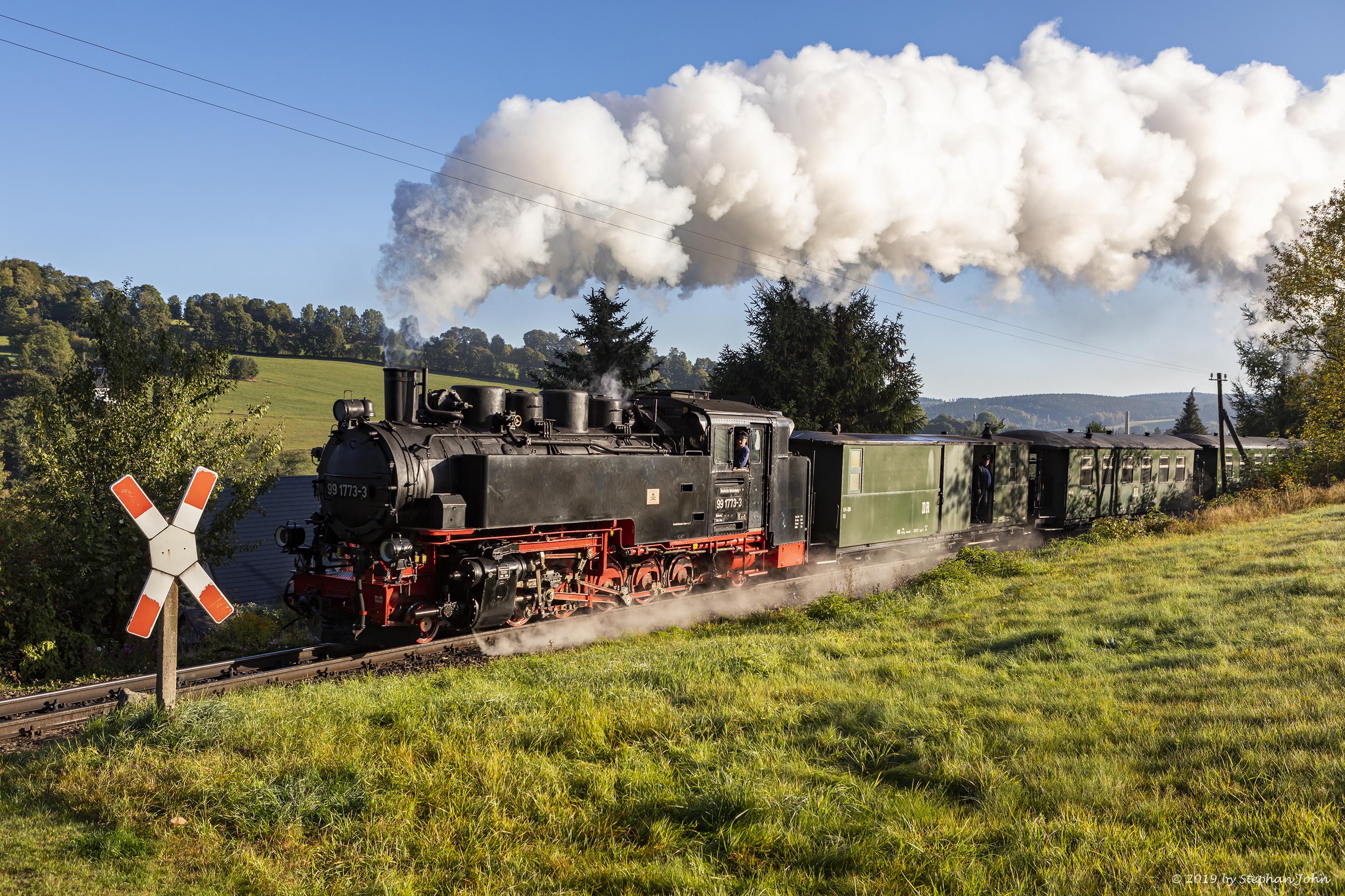 Zug 9005 mit Lok 99 1773-3 fährt mit dem Personenzug in Richtung Oberwiesenthal und passiert hier einen Bahnübergang in Neudorf.