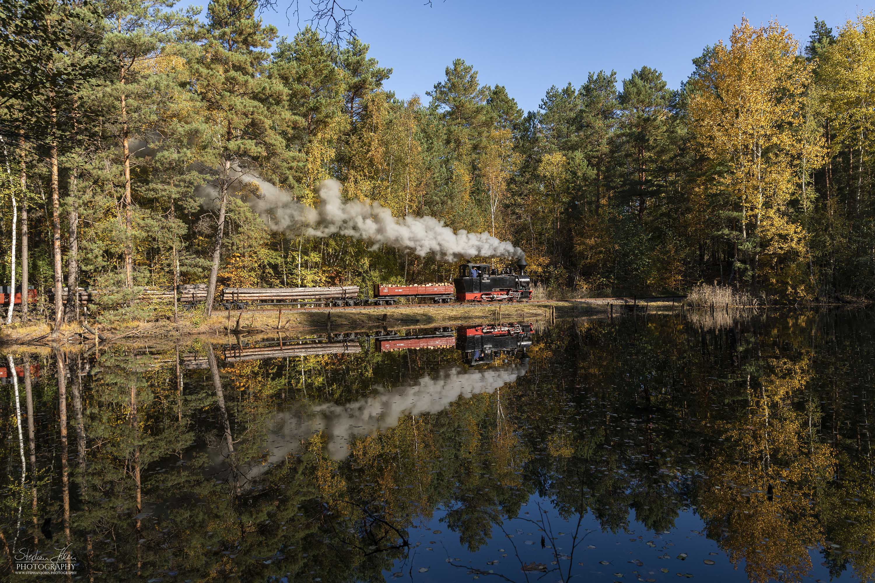 Lok 99 3312 fährt mit einem Holzzug bei bestem Wetter durch den bunten Herbstwald nach Weißwasser