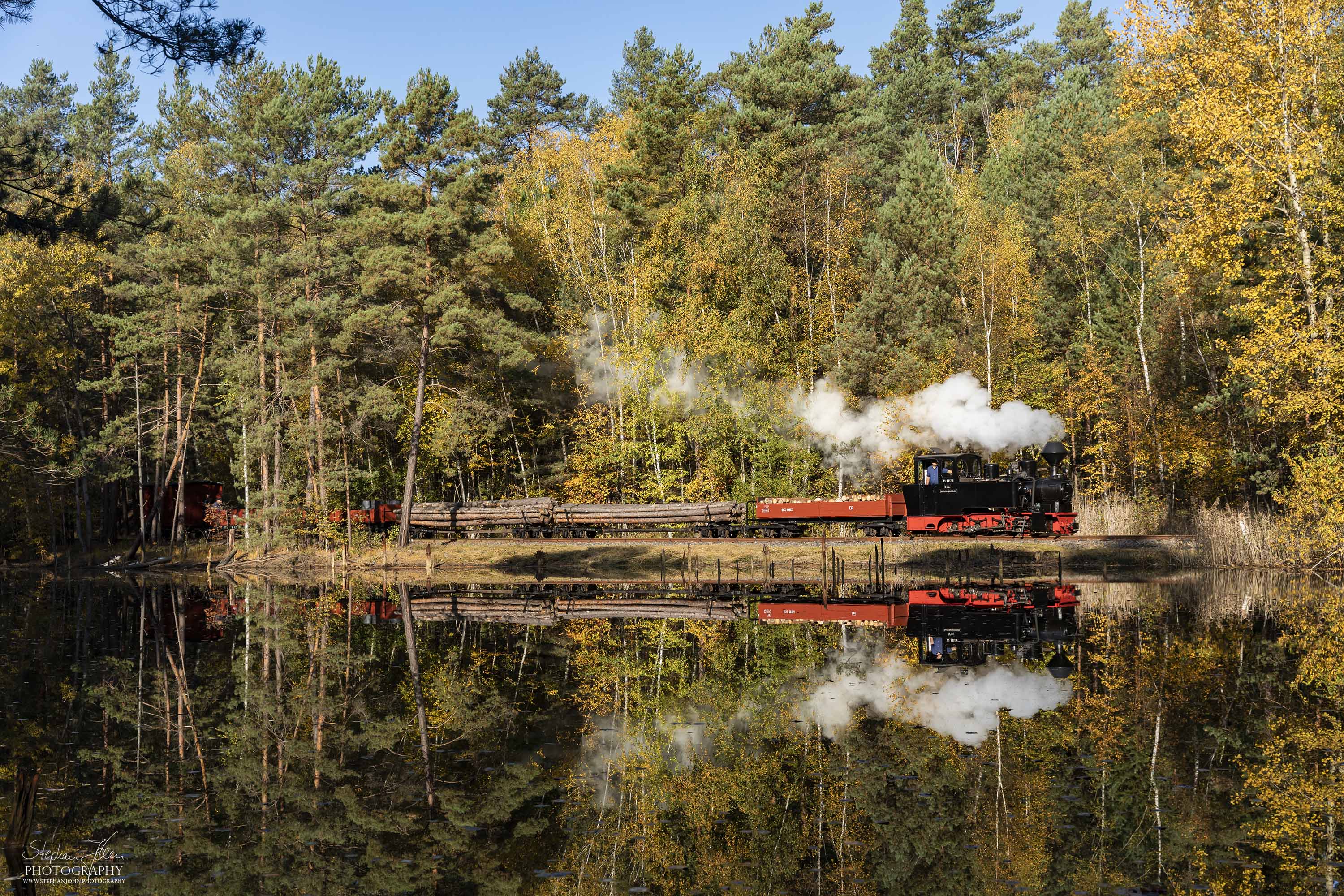 Lok 99 3312 fährt mit einem Holzzug bei bestem Wetter durch den bunten Herbstwald nach Weißwasser