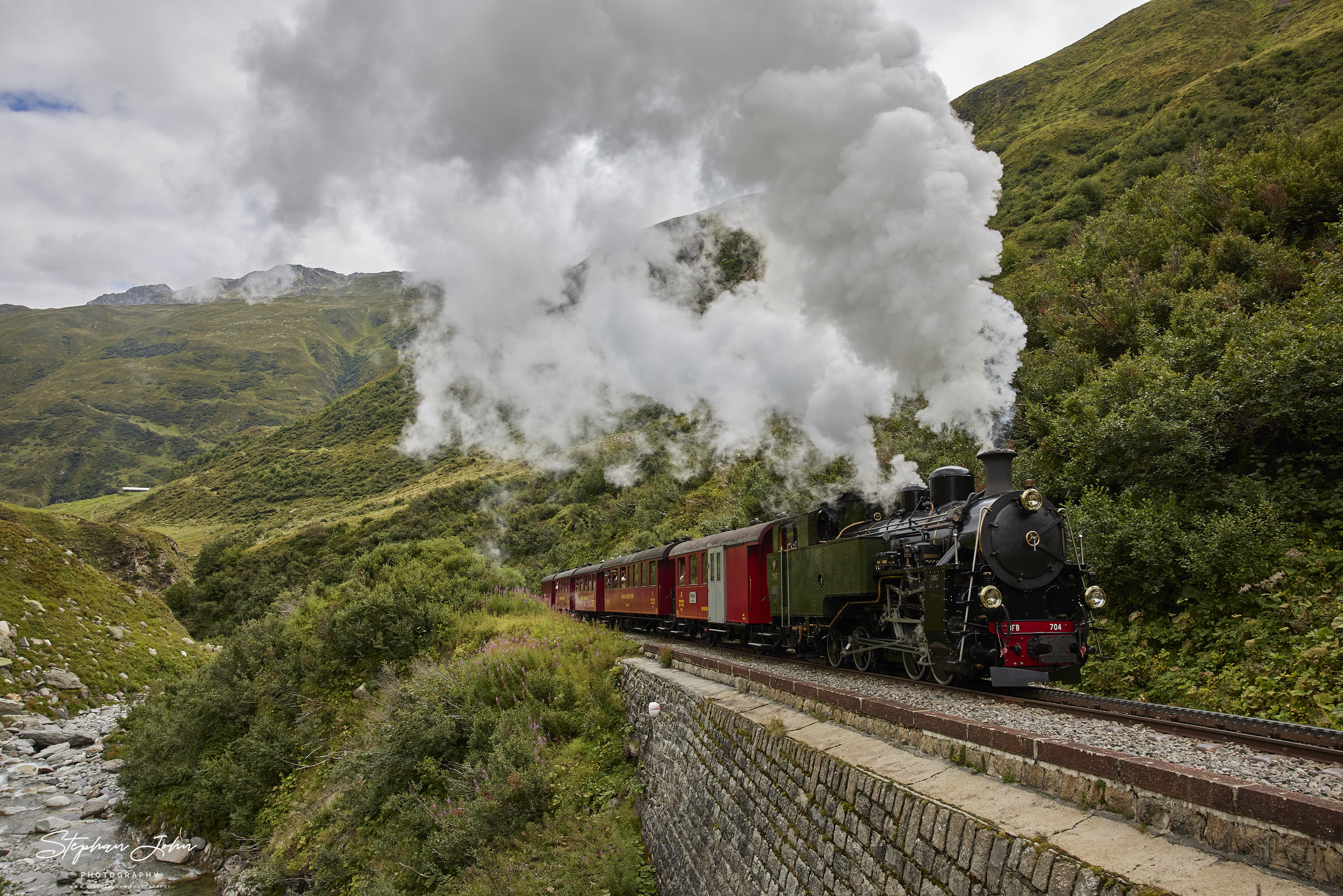 Lok 704 der DFB dampft mit einem Personenzug in Richtung Furka-Pass und Oberwald. Hier befindet sich der Zug kurz vor dem Alt Senntumstafel-Tunnel III.