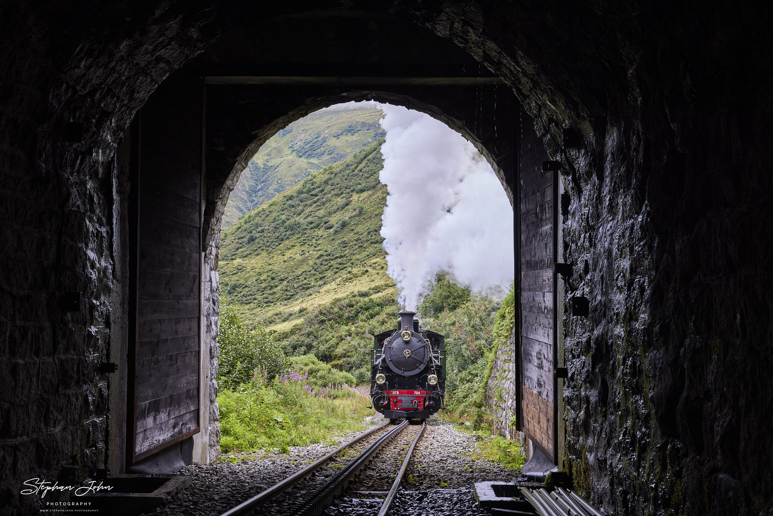 Lok 704 der DFB dampft mit einem Personenzug in Richtung Furka-Pass und Oberwald. Hier befindet sich der Zug kurz vor dem Alt Senntumstafel-Tunnel III.