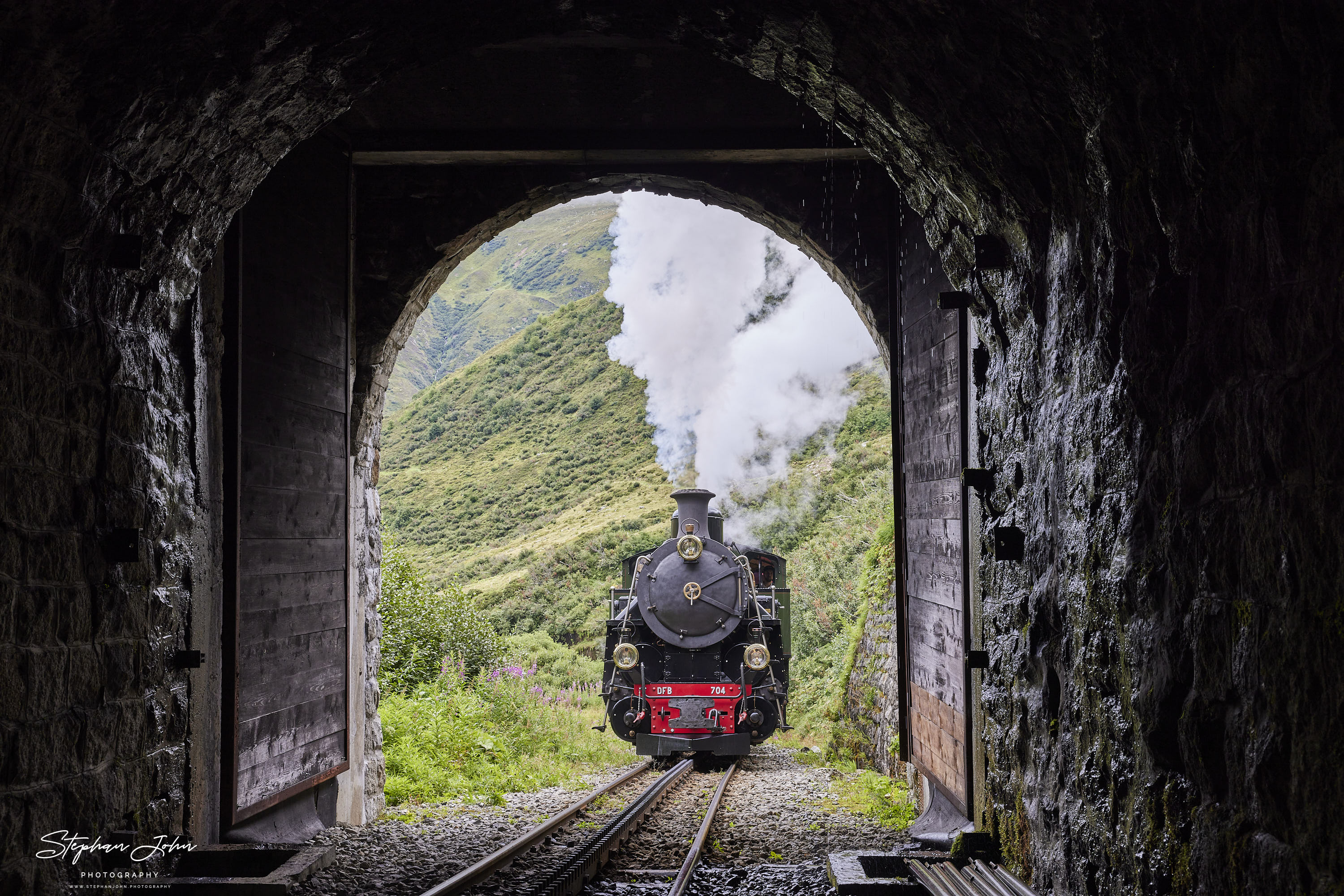 Lok 704 der DFB dampft mit einem Personenzug in Richtung Furka-Pass und Oberwald. Hier befindet sich der Zug kurz vor dem Alt Senntumstafel-Tunnel III.