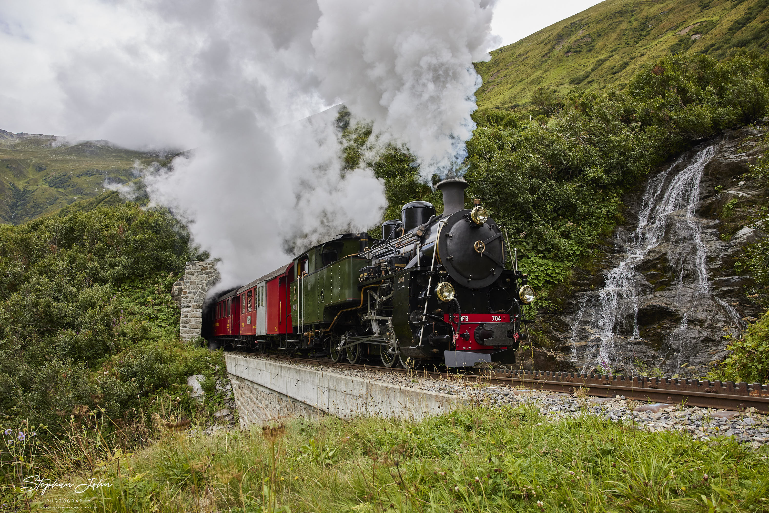 Lok 704 der DFB dampft mit einem Personenzug in Richtung Furka-Pass und Oberwald. Hier verlässt der Zug den Alt Senntumstafel-Tunnel III.