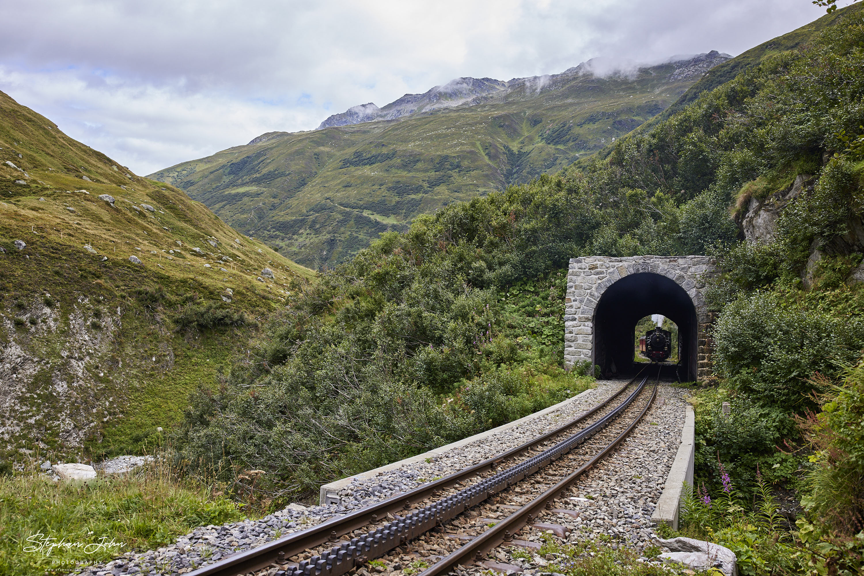 Lok 704 der DFB dampft mit einem Personenzug in Richtung Furka-Pass und Oberwald. Hier erreicht der Zug den Alt Senntumstafel-Tunnel III.