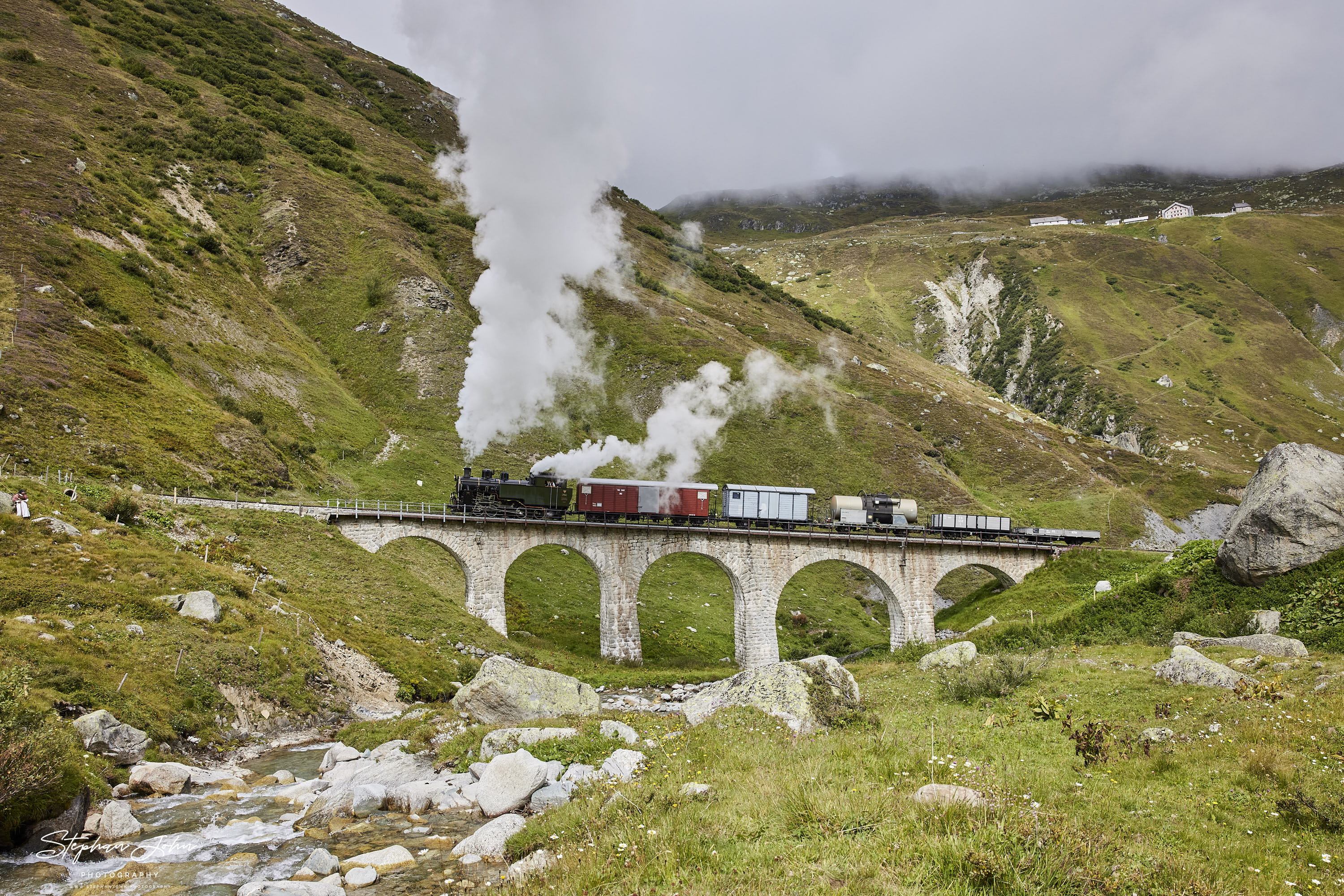 Lok 704 der DFB dampft mit einem Güterzug in Richtung Furka-Pass. Hier passiert der Zug das Steinstafelviadukt