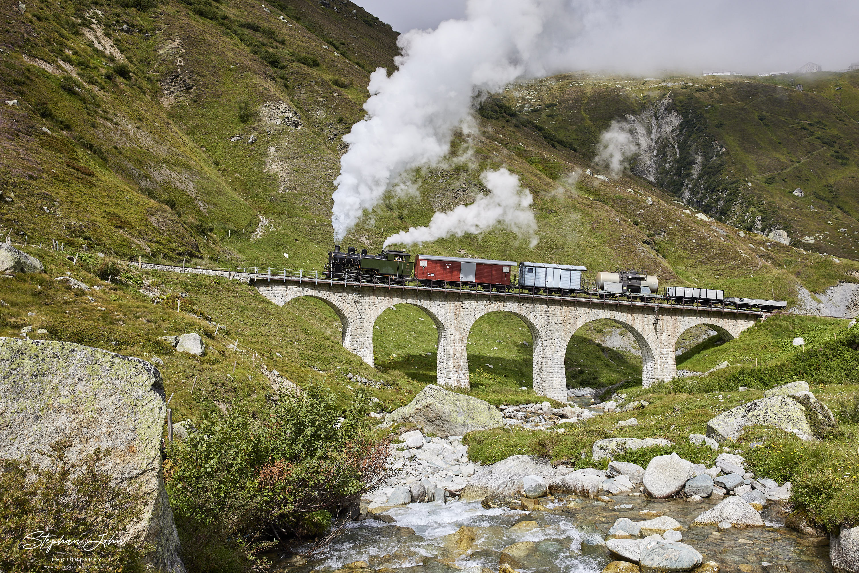 Lok 704 der DFB dampft mit einem Güterzug in Richtung Furka-Pass. Hier passiert der Zug das Steinstafelviadukt.