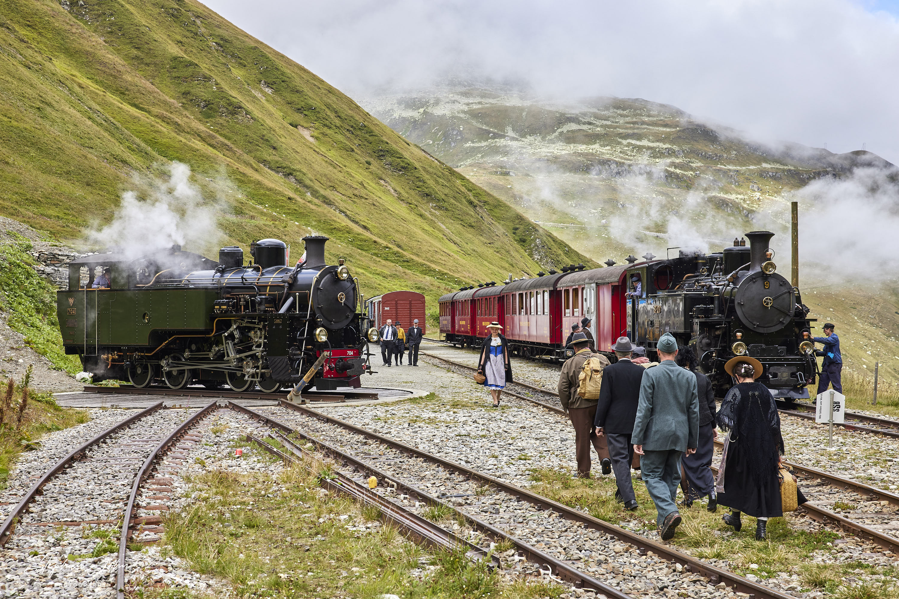 <p>Bahnhof Furka in 2.163 Meter Höhe. Der Güterzug hat abgespannt und der Personenzug nach Oberwald hat Aufenthalt. Die Reisenden nutzen die Zeit um das Drehen der Güterzuglokok anzuschauen.</p>