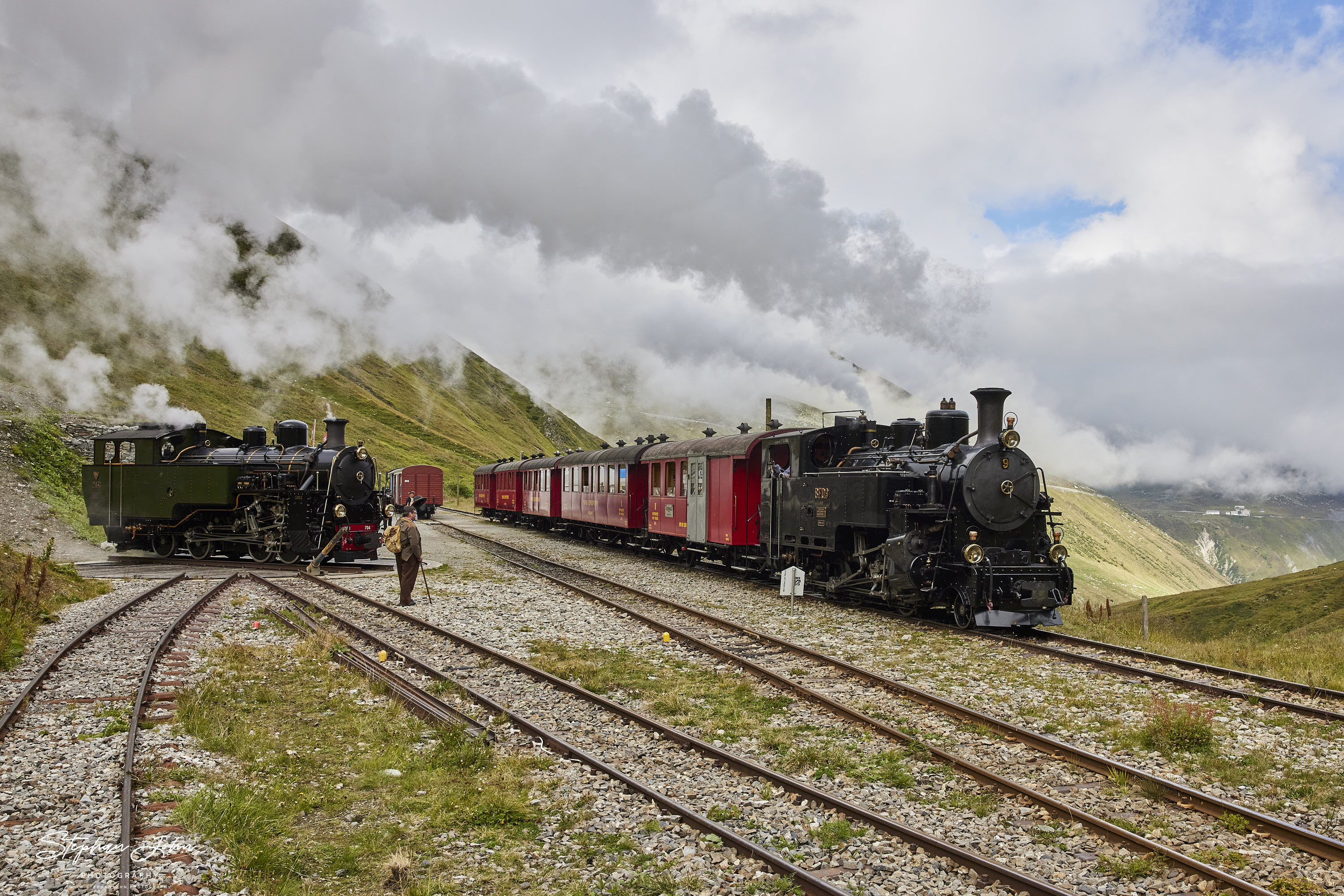 <p>Bahnhof Furka in 2.163 Meter Höhe. Der Güterzug hat abgespannt und der Personenzug nach Oberwald hat Aufenthalt. Die Reisenden nutzen die Zeit um das Drehen der Güterzuglokok anzuschauen.</p>