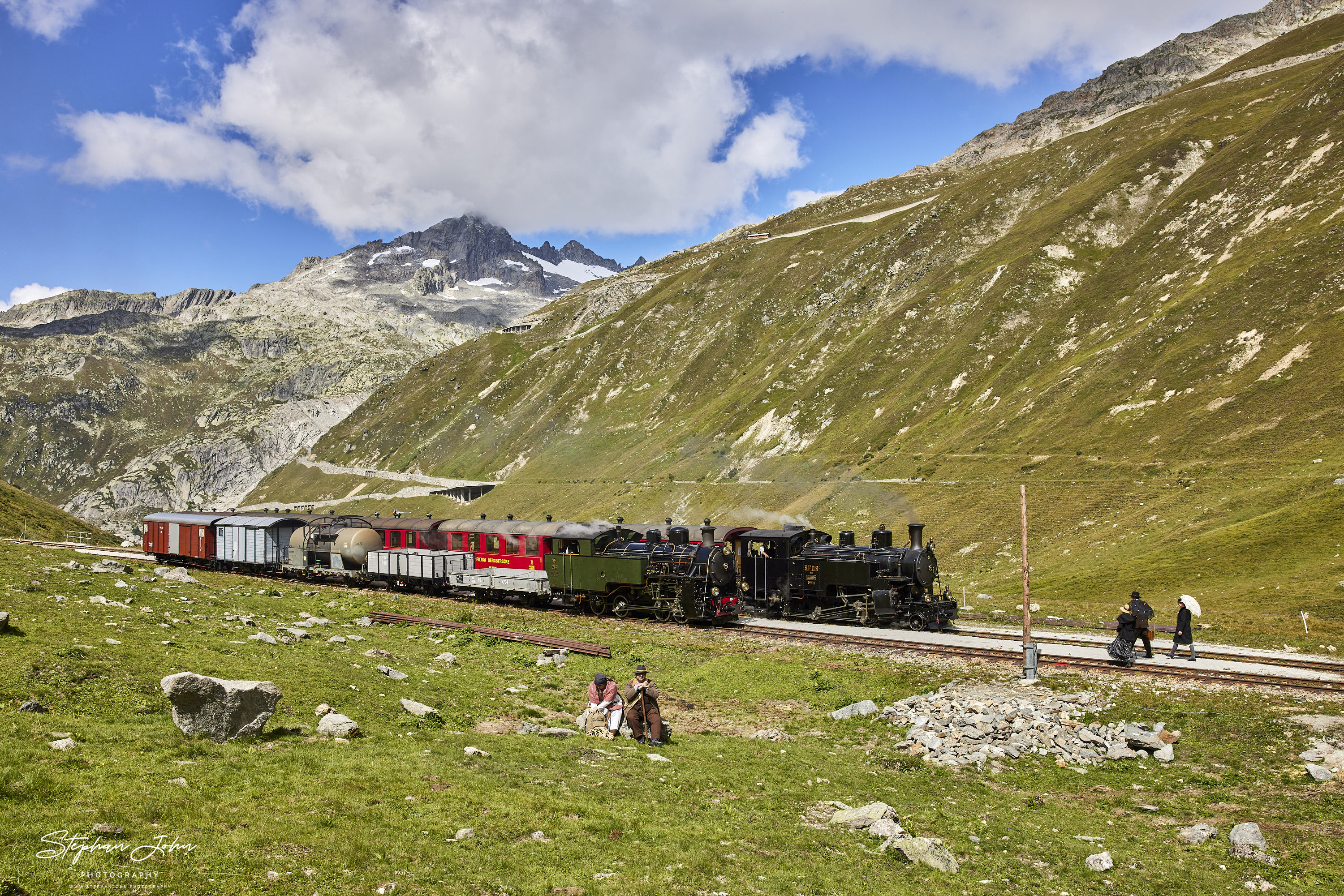 Lok 9 der DFB mit einem Personenzug und Lok 704 mit einem Güterzug haben den Bahnhof Muttbach-Belvedere (2.120 m ü. M.)erreicht und warten auf die Durchfahrt durch den Furka-Scheiteltunnel.