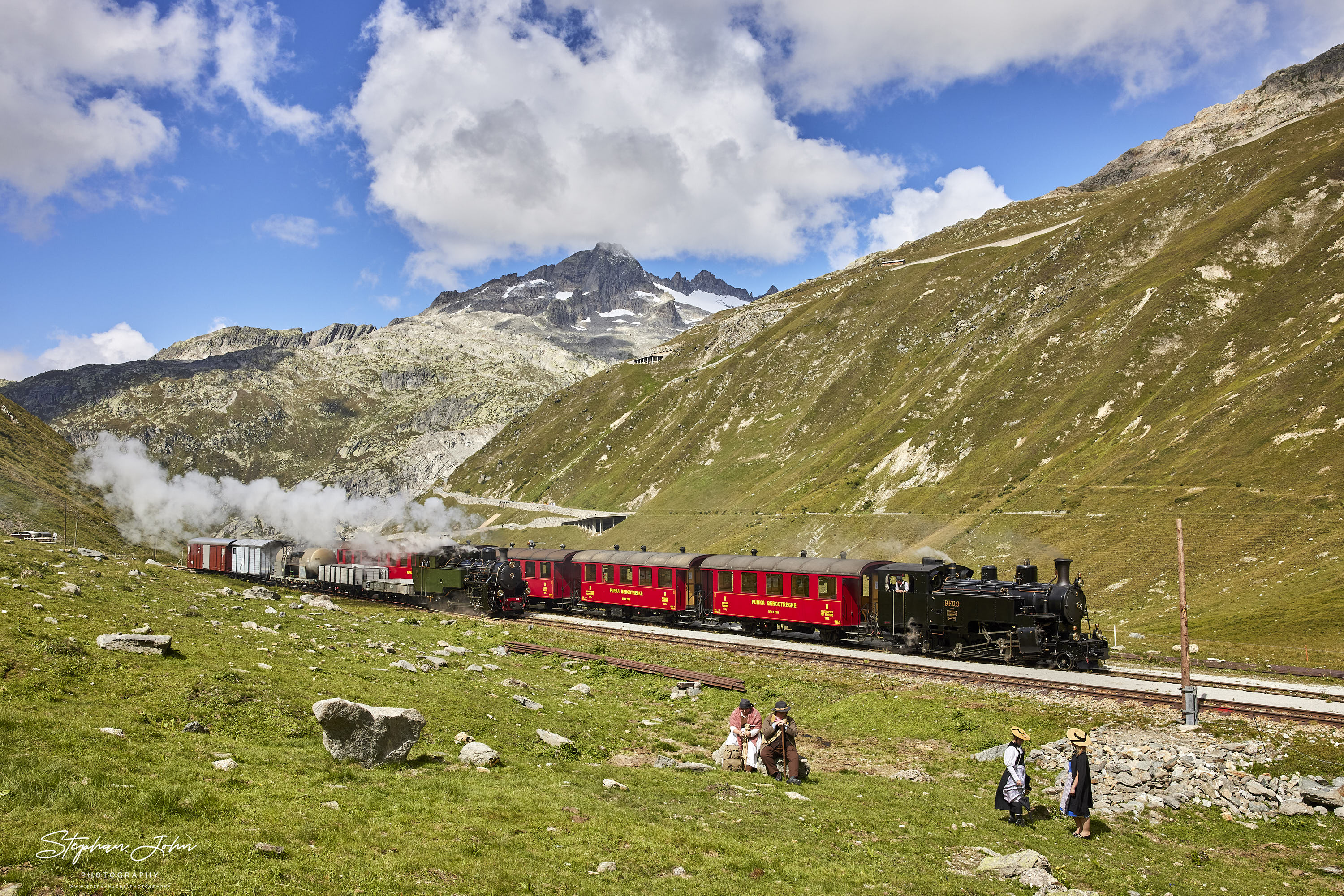 Lok 9 der DFB mit einem Personenzug und Lok 704 mit einem Güterzug haben den Bahnhof Muttbach-Belvedere (2.120 m ü. M.)erreicht und warten auf die Durchfahrt durch den Furka-Scheiteltunnel.