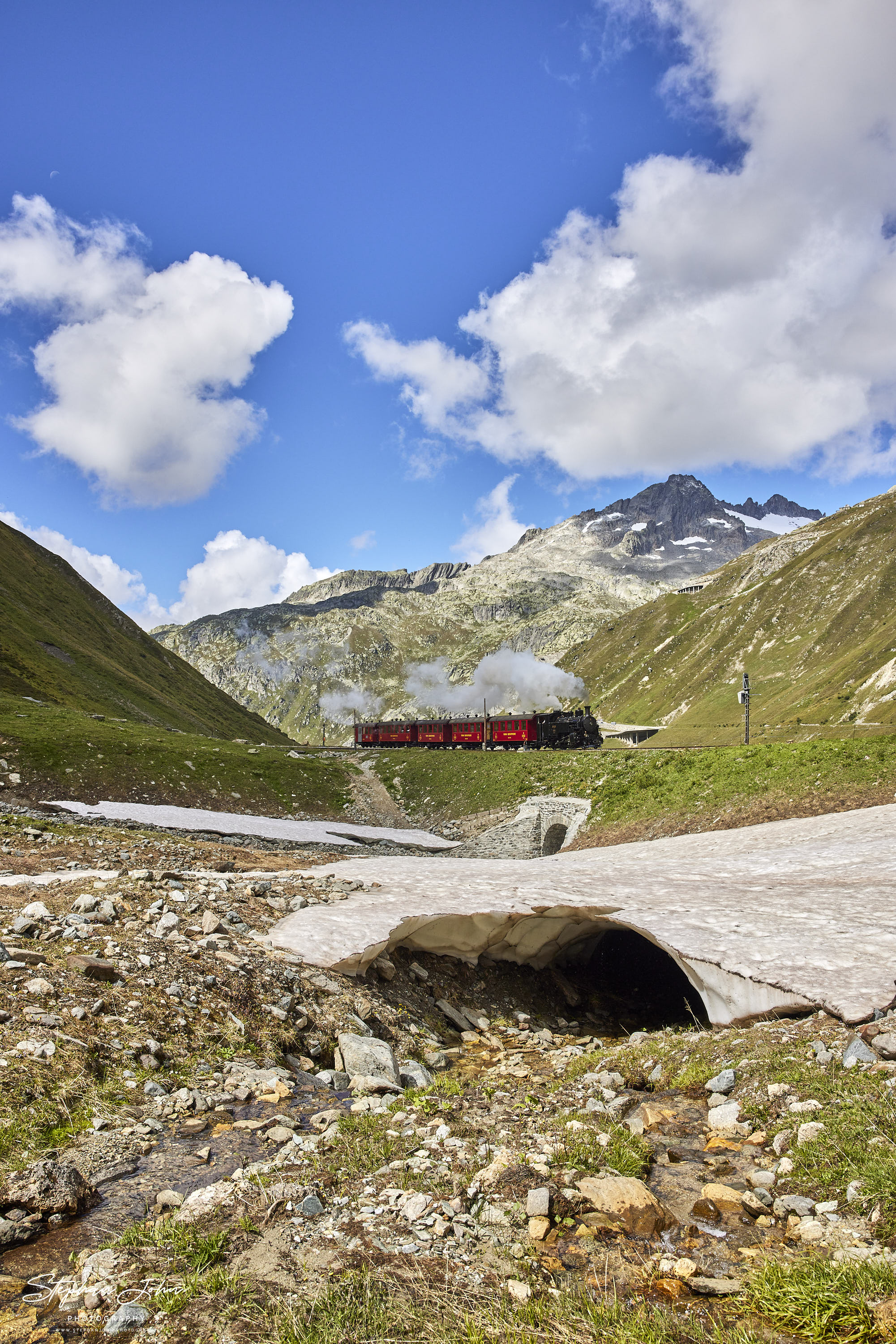 Lok 9 der DFB mit einem Personenzug fährt aus dem  Bahnhof Muttbach-Belvedere (2.120 m ü. M.) in Richtung Realp aus und verschwindet gleich im Furka-Scheiteltunnel.