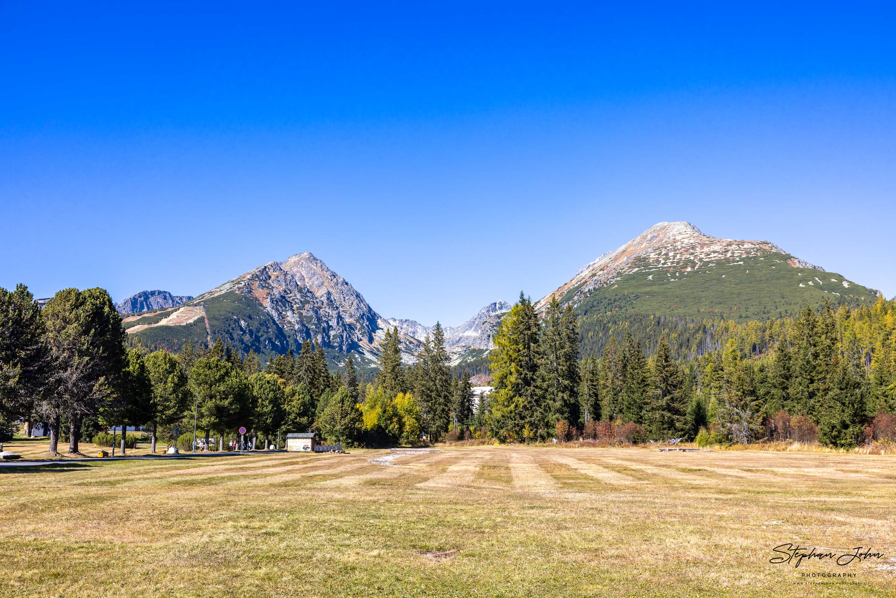 Gemähte Herbstwiese bei Štrbské Pleso vor Predné Solisko links und Patria rechts, dazwischen grüne und gelbe Bäume.