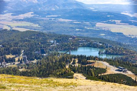 Tiefblick vom Solisko auf Štrbské Pleso mit See, Hotels, Skisprunganlagen, Wald und offenen Hängen.