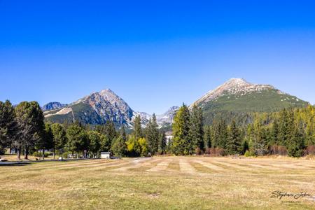 Gemähte Herbstwiese bei Štrbské Pleso vor Predné Solisko links und Patria rechts, dazwischen grüne und gelbe Bäume.
